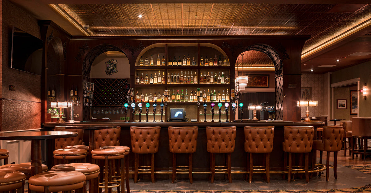 Traditional pub bar with tufted leather stools and a luxurious gold-painted pressed tin ceiling.